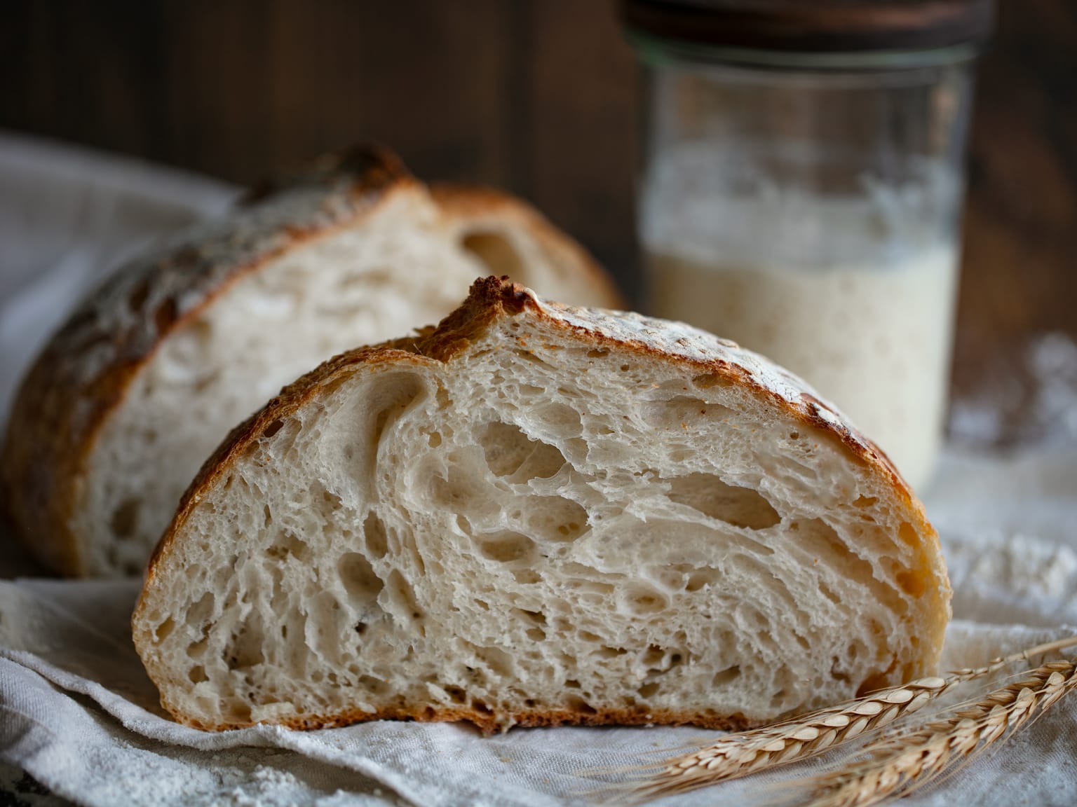 Cut sourdough loaf showing an open crumb, with a SourPod starter jar behind it